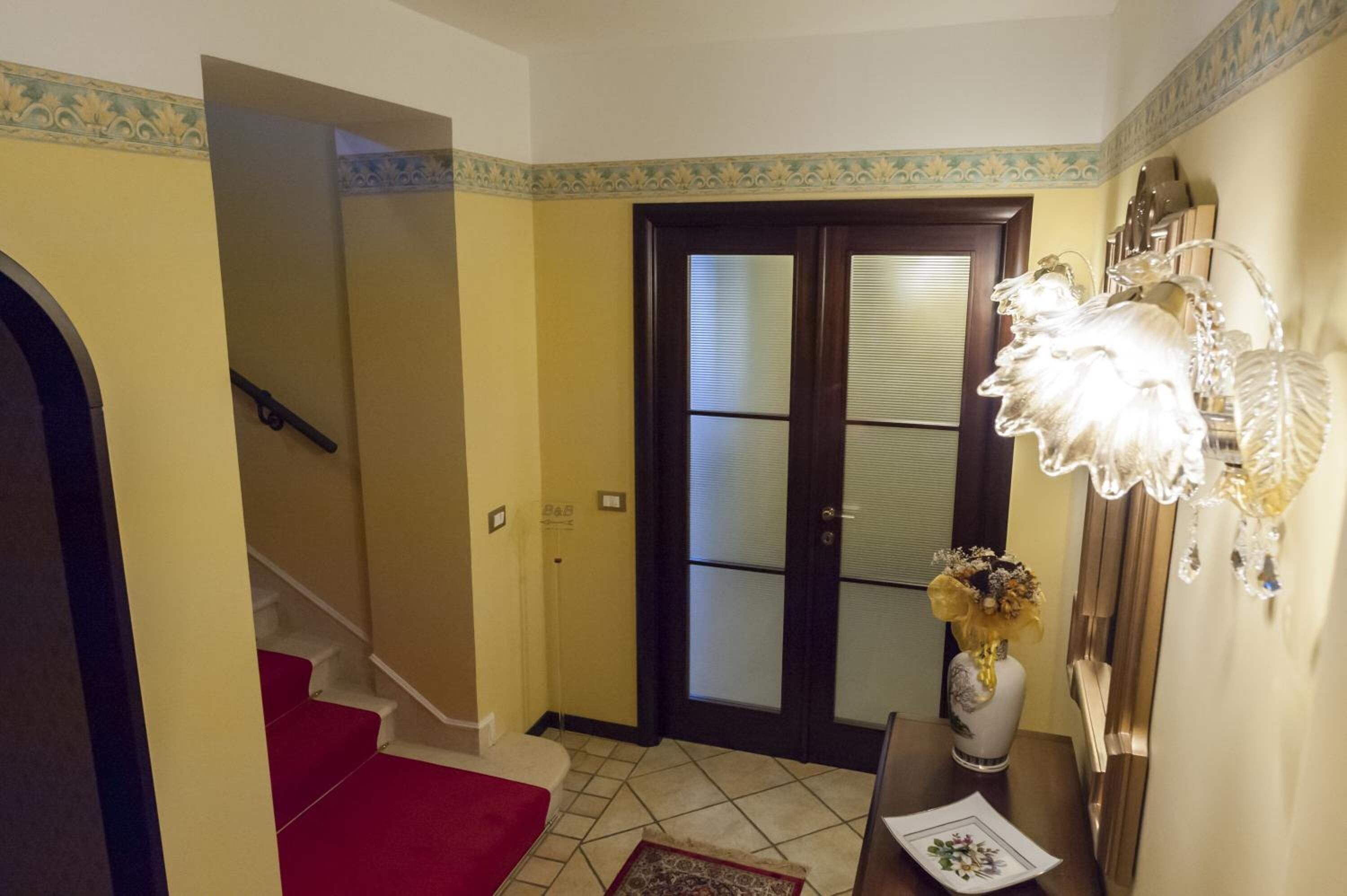 A hallway with a red carpet, a dark wooden door with glass panels, and a decorative wall fixture.