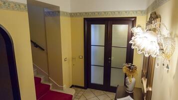 A hallway with a red carpet, a dark wooden door with glass panels, and a decorative wall fixture.