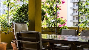 A balcony with a table and chairs, surrounded by potted plants and flowering shrubs.