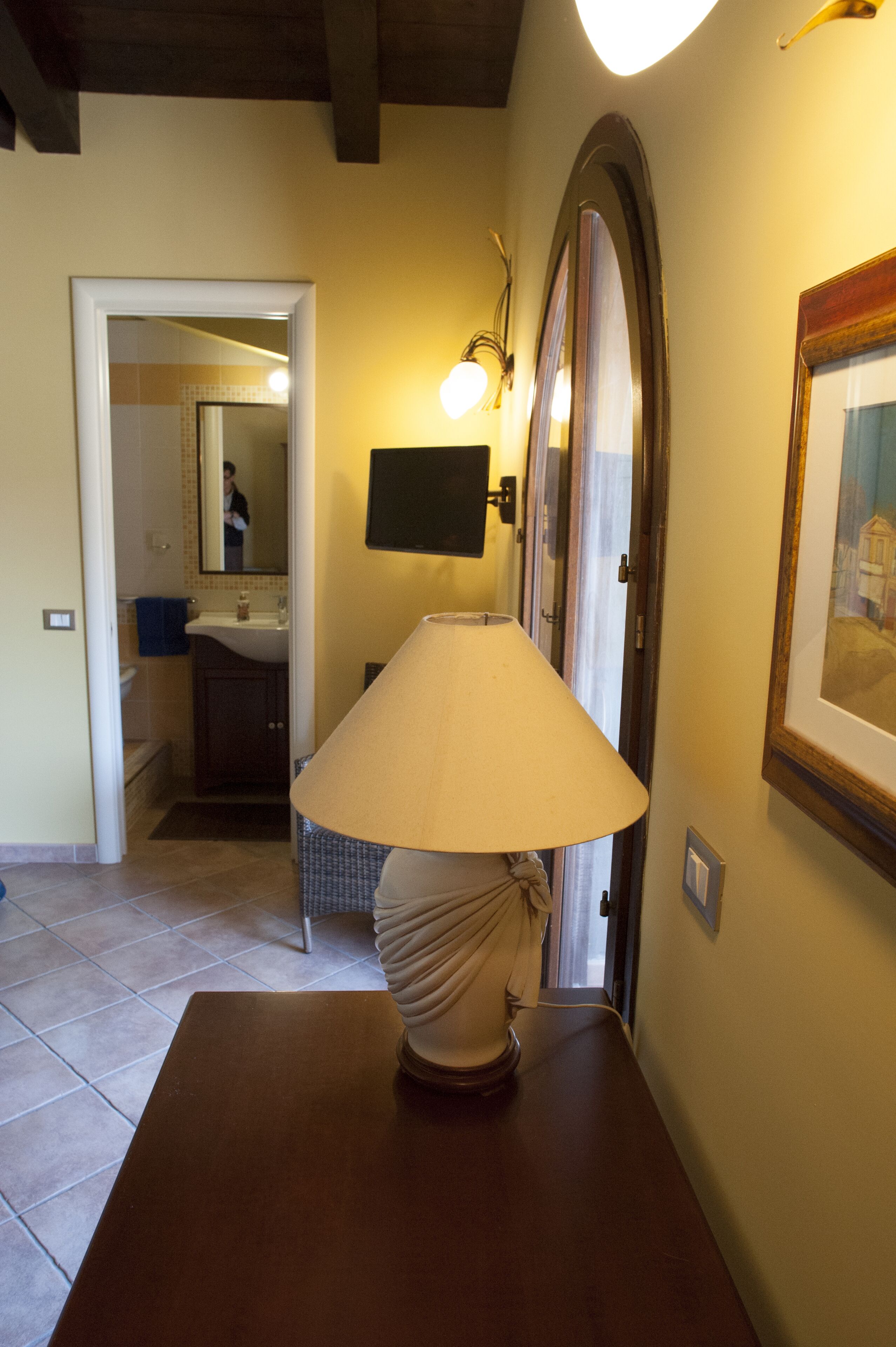 A hallway with a table lamp, a framed picture on the wall, and a doorway leading to a bathroom.