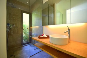A modern bathroom with a glass shower enclosure, a white sink with a chrome faucet, and a wooden vanity.