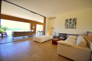 A spacious living room with a large window, a sofa, a coffee table, and a painting on the wall.