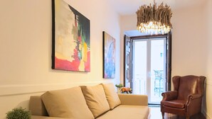 A living room with a sofa, a chair, and a potted plant. There are two paintings on the wall and a chandelier. - SantoSweethome 2 (Lisbon)