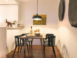 A dining area with a wooden table, black chairs, a hanging pendant light, and a sunflower painting on the wall.