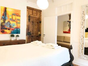 A bedroom with a large bed, a wooden door, a painting, and a mirror.