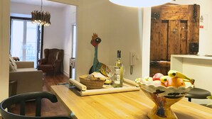 A dining area with a wooden table, chairs, a decorative bird sculpture, a bottle of wine, and a bowl of fruit. - SantoSweethome 2 (Lisbon)