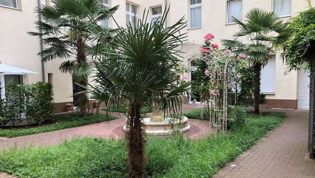 A courtyard with palm trees, a fountain, and a brick pathway. - Super * * * * * * Apartment at the main station with terrace, WiFi, washing machine.  (Berlin)