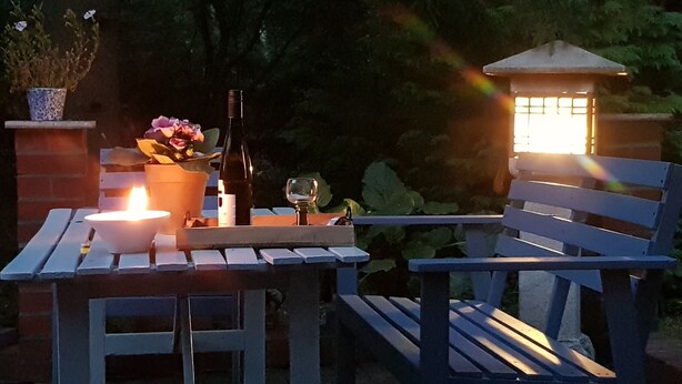 Un patio con una mesa, una silla, una vela, una botella y una copa.