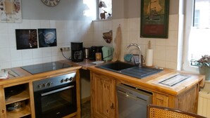 Una cocina compacta con armarios de madera, horno empotrado, lavavajillas y fregadero. Hay un reloj en la pared y un cuadro enmarcado sobre el fregadero.