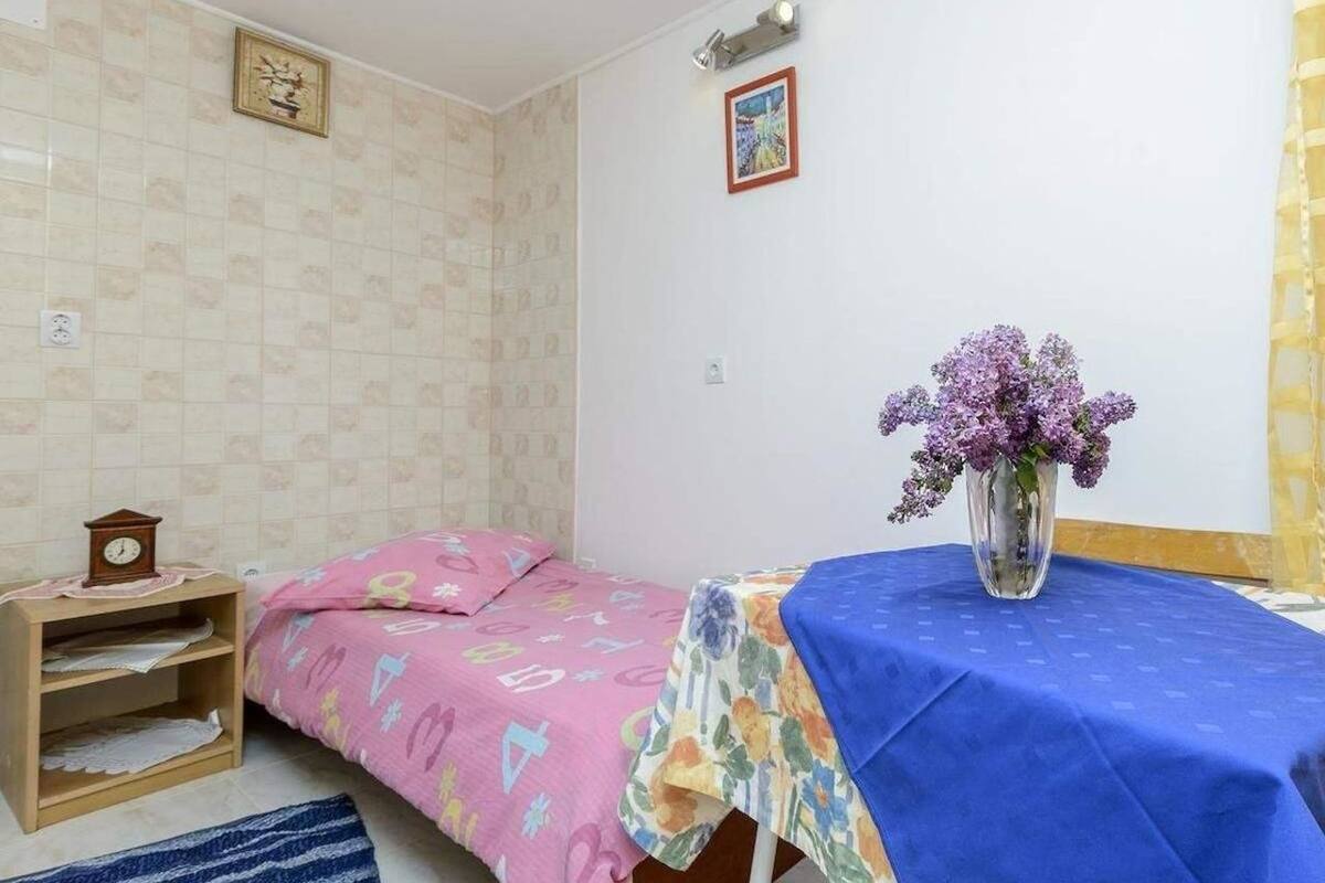 Um quarto com cama, mesa de cabeceira, uma mesa com um vaso de flores e um relógio na parede.