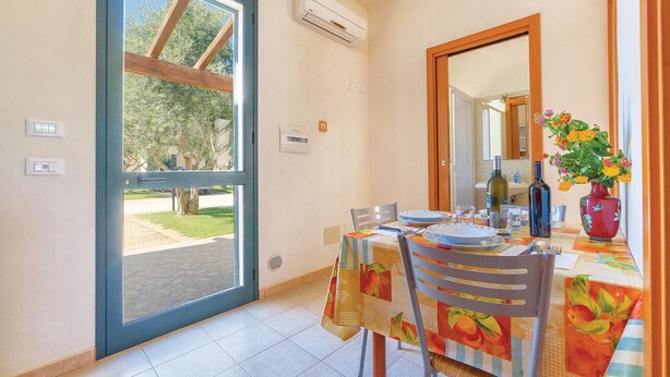Uma área de refeições com uma mesa posta para dois, uma janela com vista para árvores e um aparelho de ar condicionado na parede.