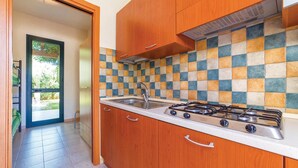 Uma cozinha com armários de madeira, painel de azulejos, pia de aço inoxidável e fogão a gás.