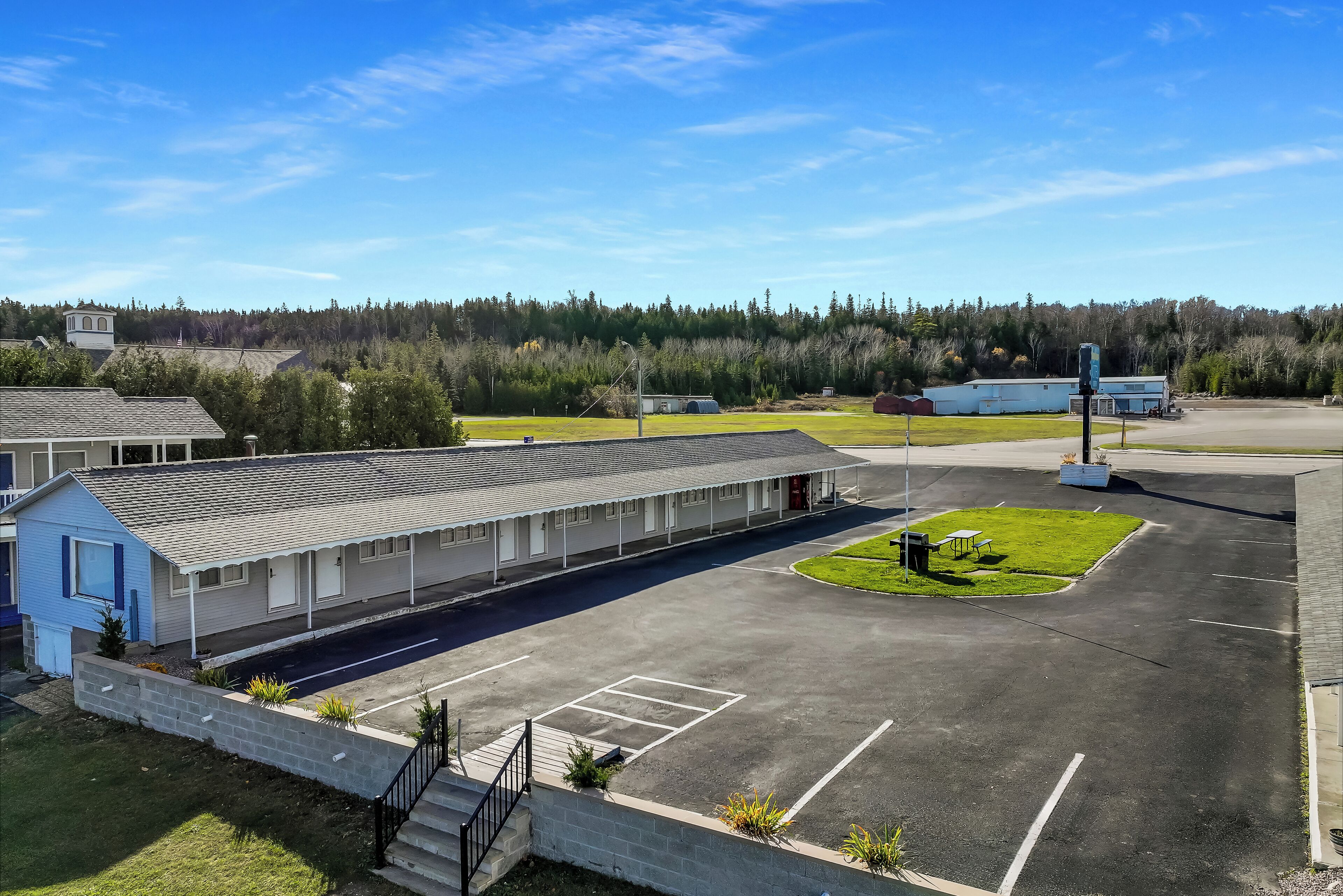 A motel with a parking lot, a small grassy area, and a forested background.