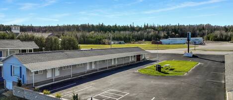 A motel with a parking lot, a small grassy area, and a forested background.
