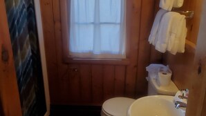 A small, wooden-paneled bathroom with a toilet, sink, and window. - Bayview Lakefront Motel (St Ignace)