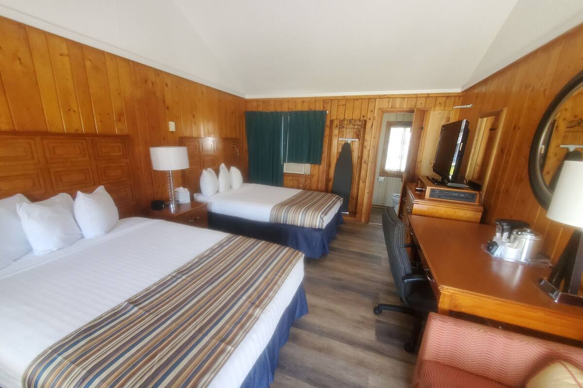 Quarto de hotel com duas camas, uma mesa com cadeira, televisão e espelho.