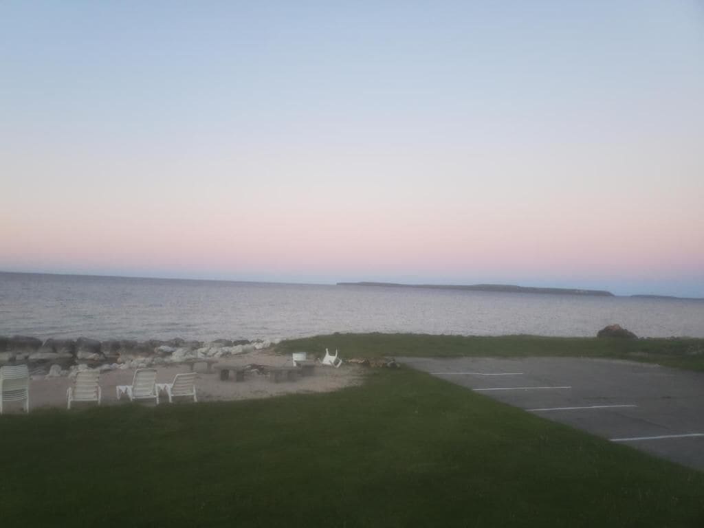 A parking lot with a view of the ocean and a grassy area with white chairs.
