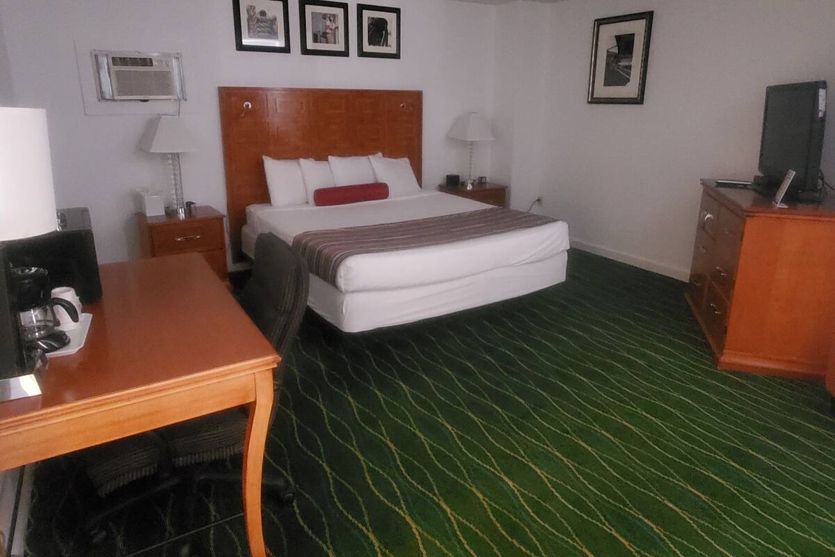 Quarto de hotel com uma cama, escrivaninha, cadeira, cômoda e televisão.