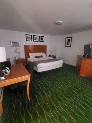 A hotel room with a bed, a desk, a chair, a dresser, and a television. - Bayview Lakefront Motel (St Ignace)