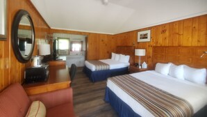A hotel room with wooden paneling, a bed, a desk with a chair, a small sofa, a mirror, and a ceiling fan. - Bayview Lakefront Motel (St Ignace)