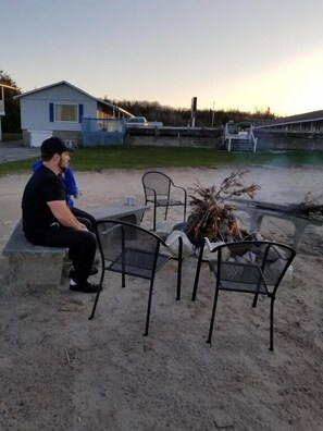 A sandy outdoor area with a fire pit and metal chairs. - Bayview Lakefront Motel (St Ignace)