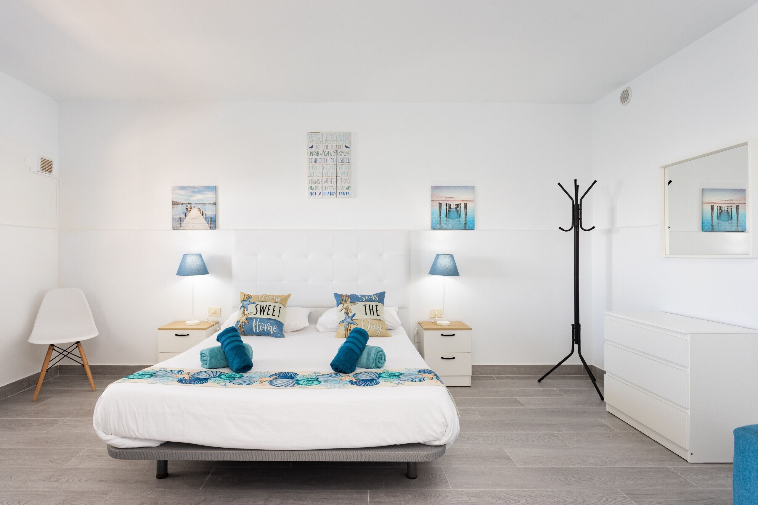 Une chambre à coucher moderne avec un grand lit, deux tables de chevet avec des lampes, un porte-manteau et des œuvres d’art accrochées aux murs.