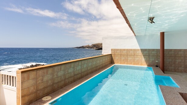 A swimming pool with a view of the ocean, a ceiling fan, and a tiled wall. - Coastal Dream with heatable pool (Güimar)