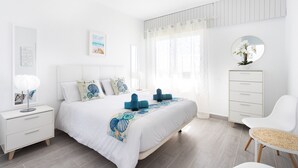 A modern bedroom with a large bed, white walls, a wooden floor, a bedside table with a lamp, a chair, and a dresser. - Coastal Dream with heatable pool (Güimar)