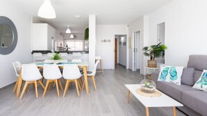 A modern living room with a grey sofa, a dining table with white chairs, and a kitchen in the background. - Coastal Dream with heatable pool (Güimar)