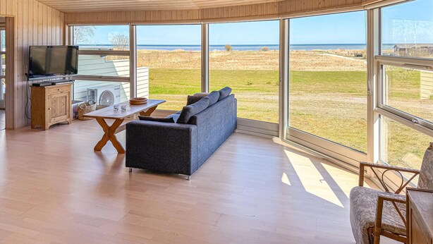 A modern living room with a large window, a sofa, a TV, and a wooden cabinet. - Amazing home in ørsted with kitchen (Ørsted)