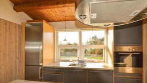 A modern kitchen with stainless steel appliances, wooden cabinets, and a large window providing a view of the outdoors. - Amazing home in ørsted with kitchen (Ørsted)