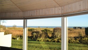 A room with large windows offering a view of a grassy field and the sea. - Amazing home in ørsted with kitchen (Ørsted)