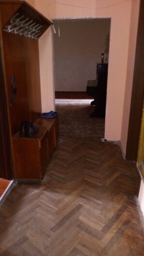 A hallway with a herringbone floor pattern, a wooden bench with shoes, and a dark-colored cabinet. - Family Hostel (Batumi)