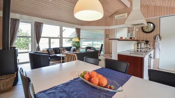 A cozy room with a dining table, chairs, a sofa, and a kitchen area with a clock and a kettle. - Awesome home in Ebeltoft with sauna (Ebeltoft)
