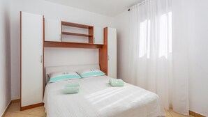 A bedroom with a bed, a built-in shelf above the bed, and a window with curtains. - Amazing apartment in Omisalj with WiFi (Omisalj)