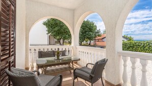 A covered outdoor seating area with a table and chairs, white balustrades, and a view of the sea. - Amazing apartment in Omisalj with WiFi (Omisalj)