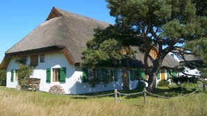 Une maison traditionnelle avec un toit de chaume, des murs blancs et des volets verts.