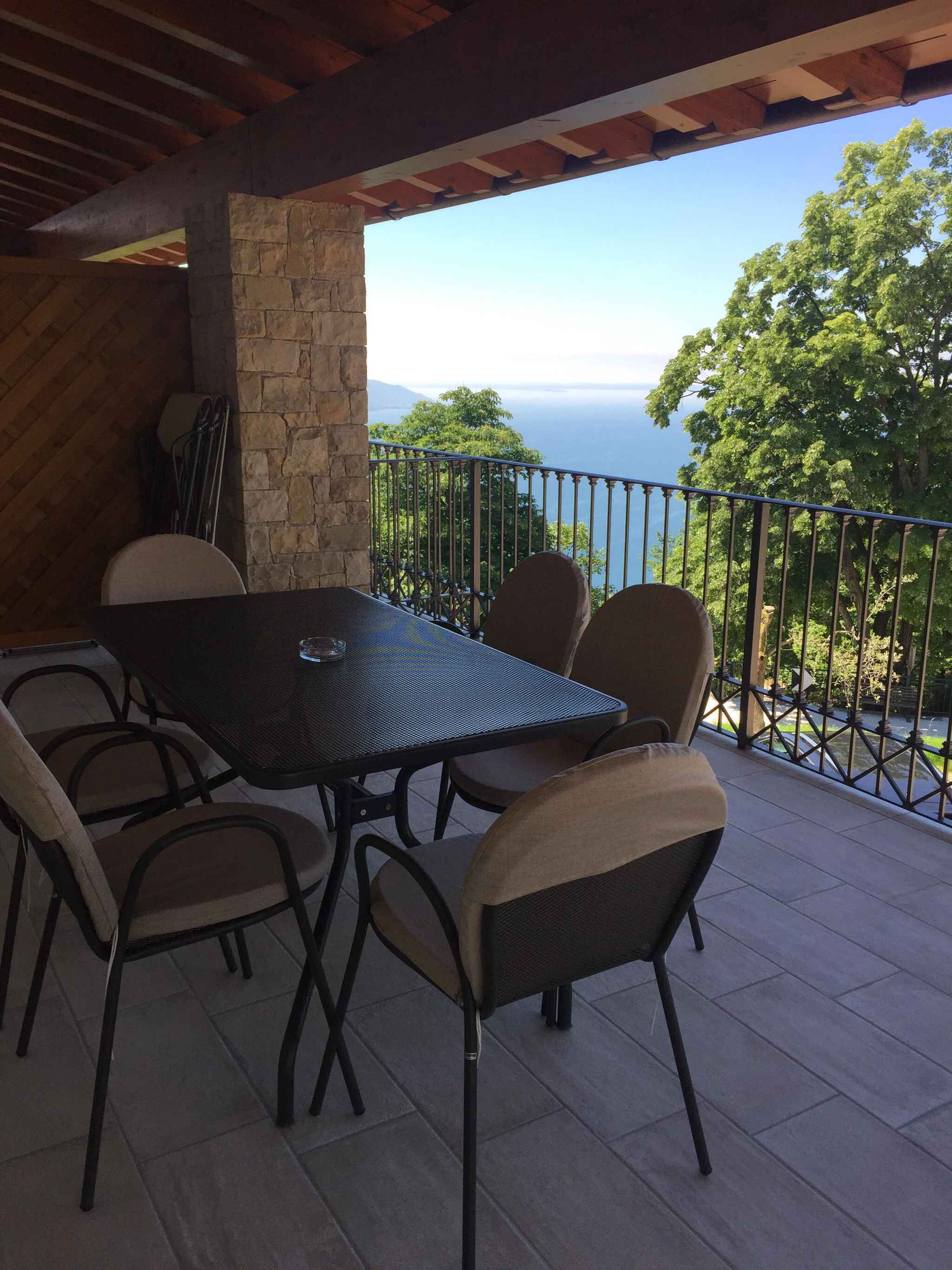 Un patio al aire libre con una mesa, sillas, un pilar de piedra y vista al mar.
