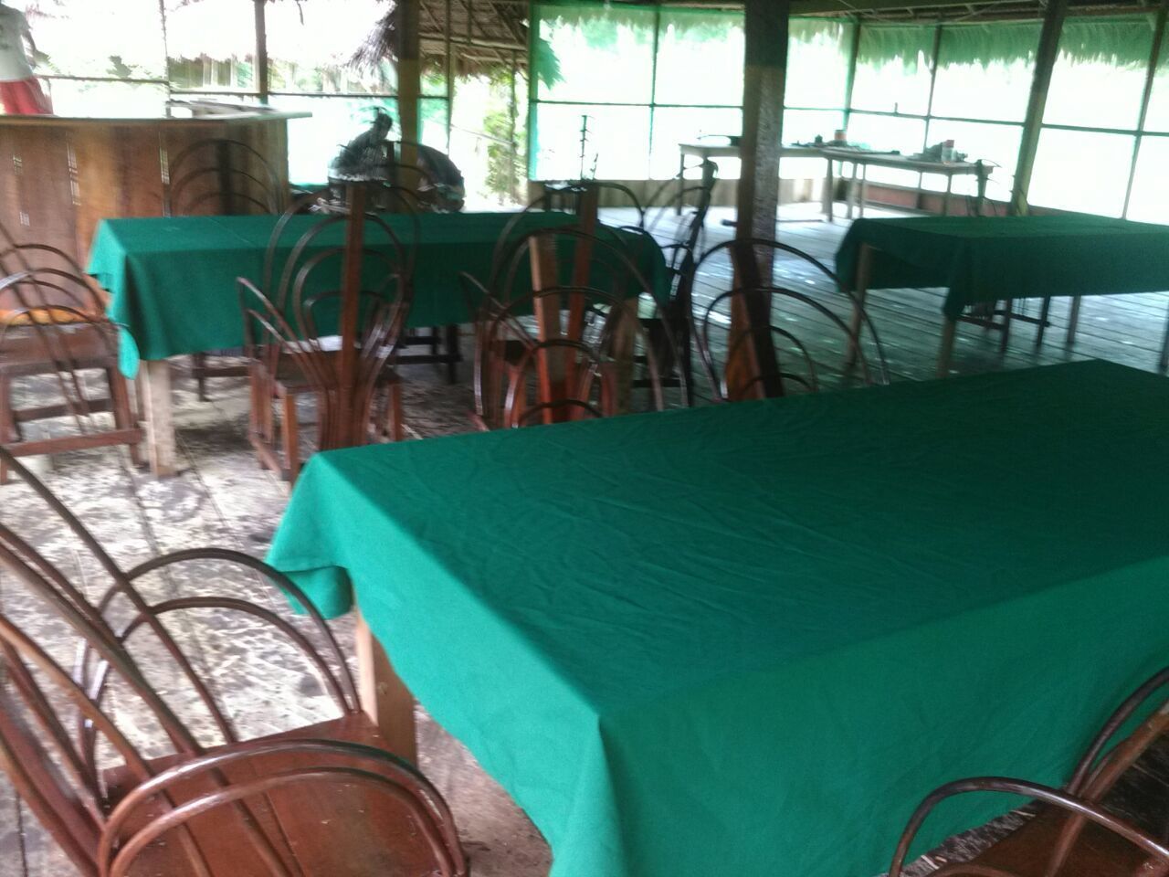 A dining area with tables covered in green tablecloths and metal chairs.