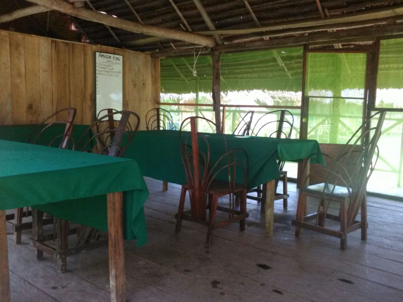 A covered outdoor dining area with tables and chairs, a wooden wall, and a signboard.