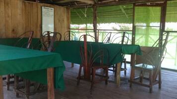 A covered outdoor dining area with tables and chairs, a wooden wall, and a signboard.