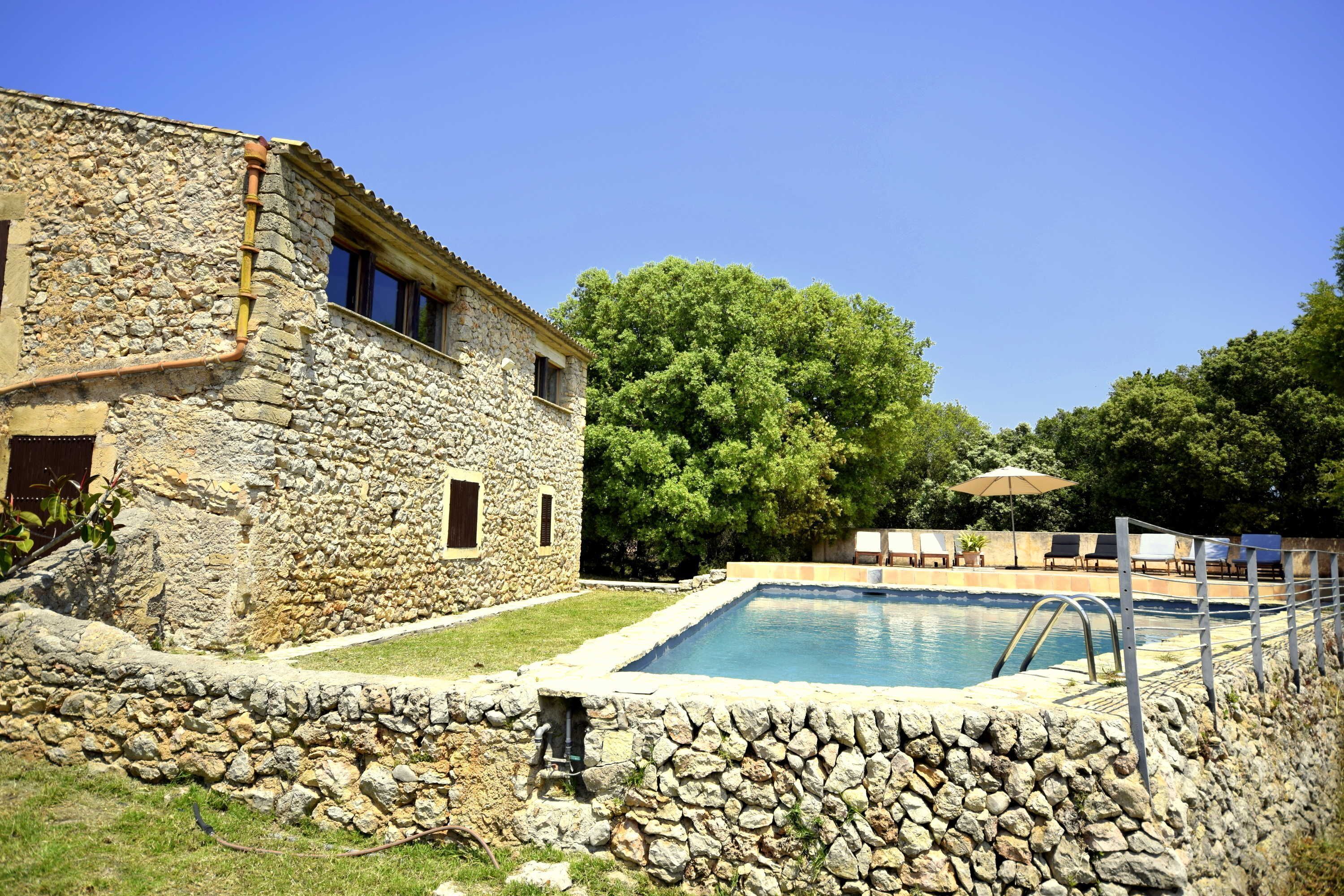 A stone building with a pool, surrounded by a stone wall and greenery.
