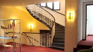 Eine Hotelhalle mit einer Wendeltreppe, einem roten Teppich und einem Metallregal mit Gegenständen darauf.