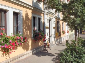 Um edifício com fachada amarela, janelas grandes e caixas de flores no andar térreo.