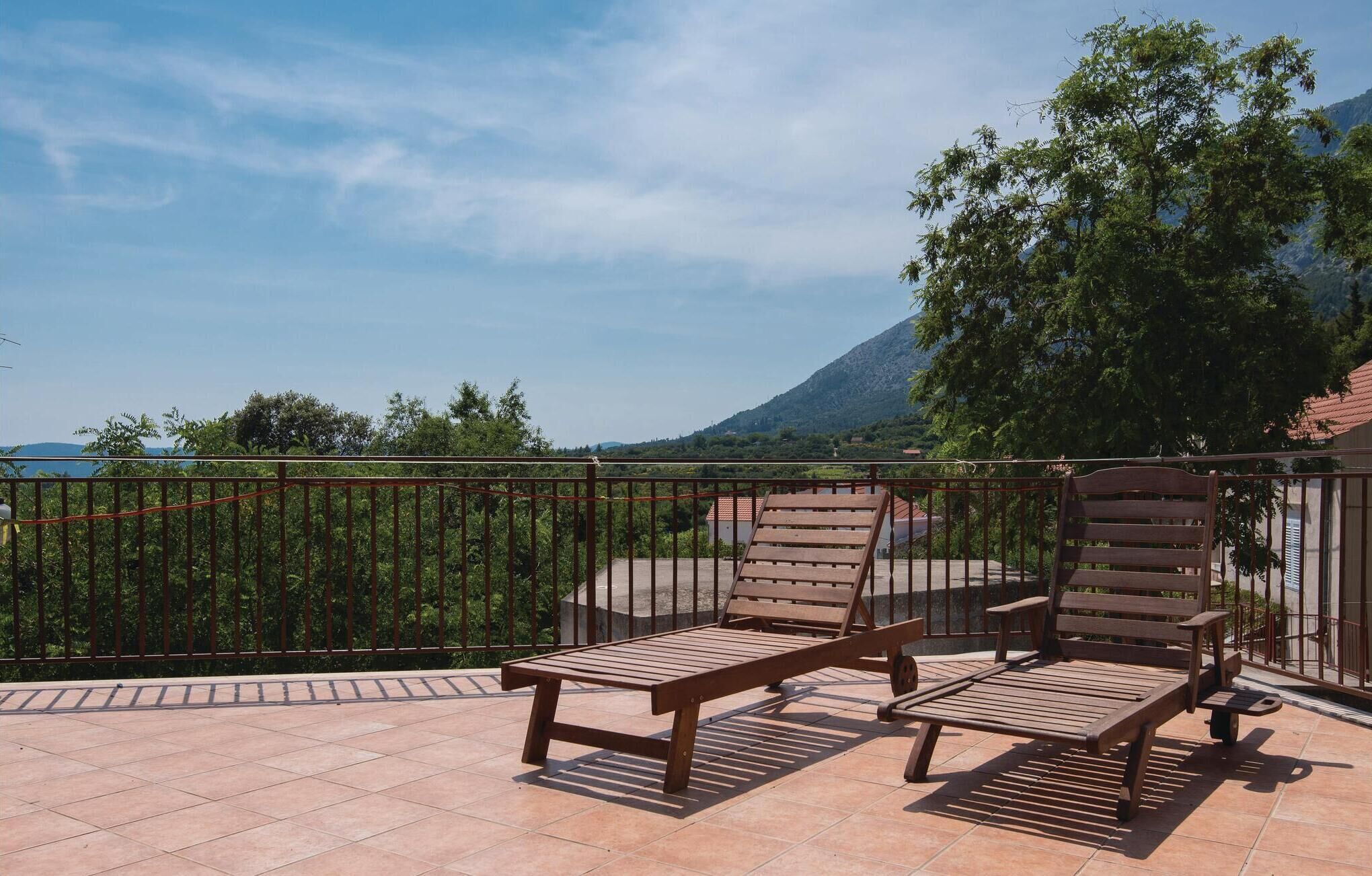 A terrace with two wooden lounge chairs and a table, overlooking a mountainous landscape.