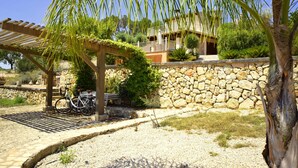 A stone wall, a pergola with climbing plants, a bicycle, and a building with a balcony in the background. - 750139 Sa Font near Petra (license ETV/941) - 750139 Sa Font (Petra)