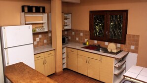 A compact kitchen with wooden cabinets, a built-in sink, and a refrigerator. - Manaona Guest House (Antananarivo)