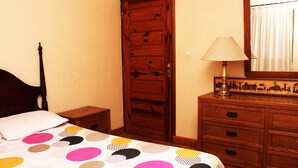 A bedroom with a bed, a wooden nightstand, a dresser with drawers, a lamp, and a mirror. - Manaona Guest House (Antananarivo)