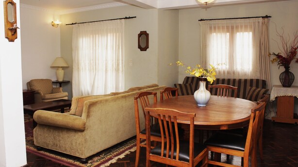 A dining area with a wooden table and chairs, a sofa, a lamp, and a vase with flowers. - Manaona Guest House (Antananarivo)