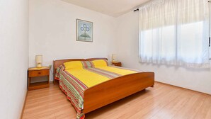 Un dormitorio con una cama de madera, una mesita de noche con lámpara y una ventana con cortinas traslúcidas.
